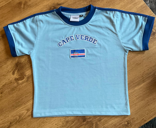 Light blue t-shirt with 'Cape Verde' text and flag on a wooden surface