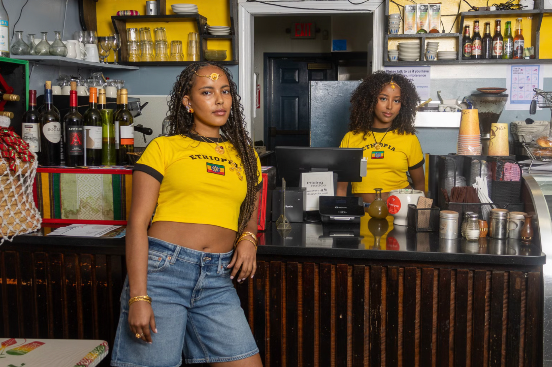 Two women in yellow shirts standing behind a counter in a bar or restaurant.