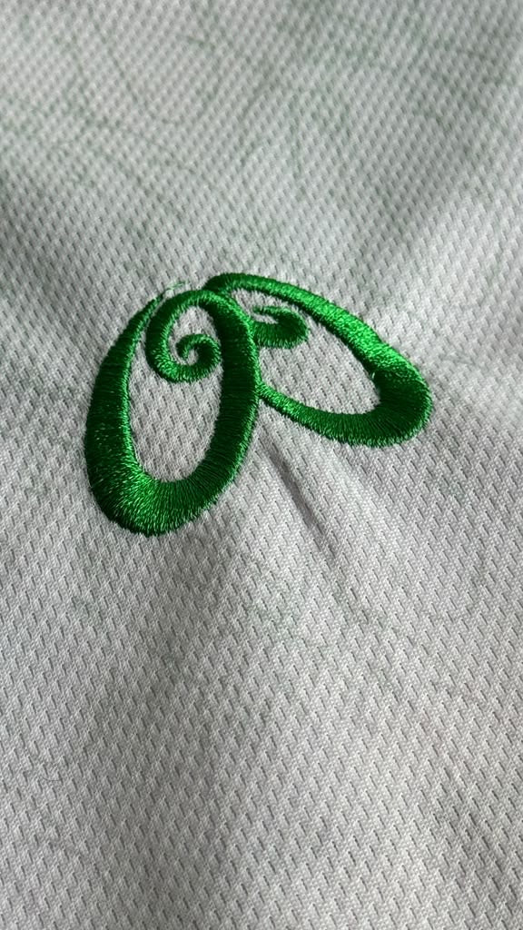 A close-up of a white textured fabric with a bright green embroidered cursive swirl logo.