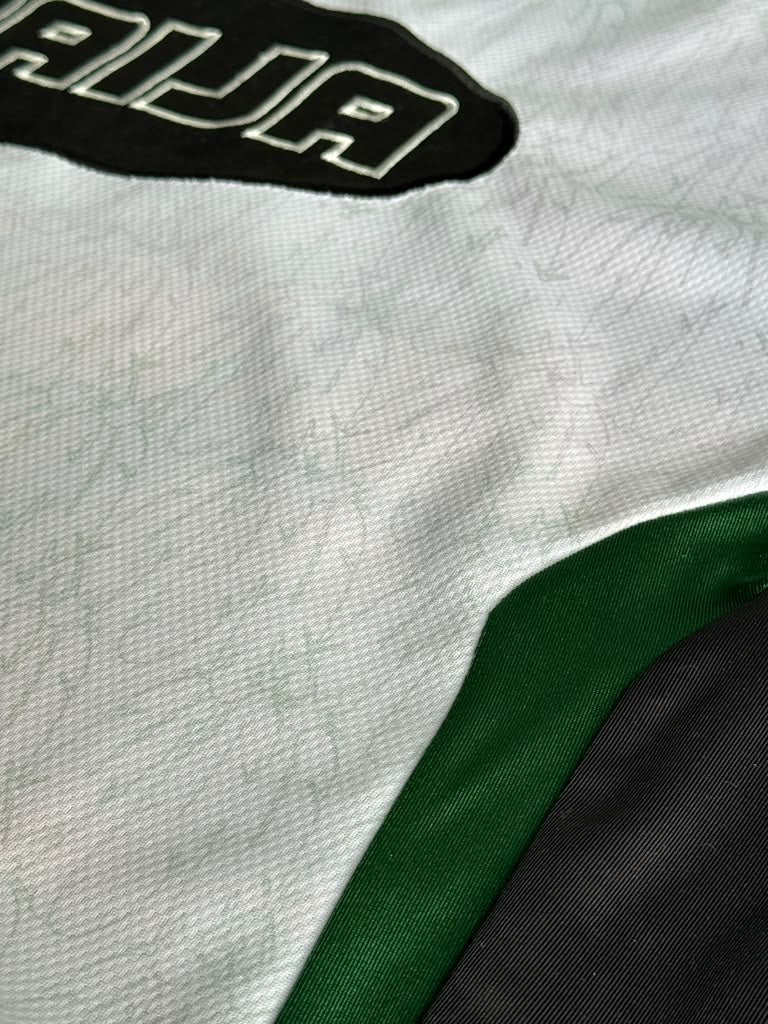 Close-up of a white athletic jersey with a black patch containing the letters 'AIJA' in white, a green side panel, and a black lower section.