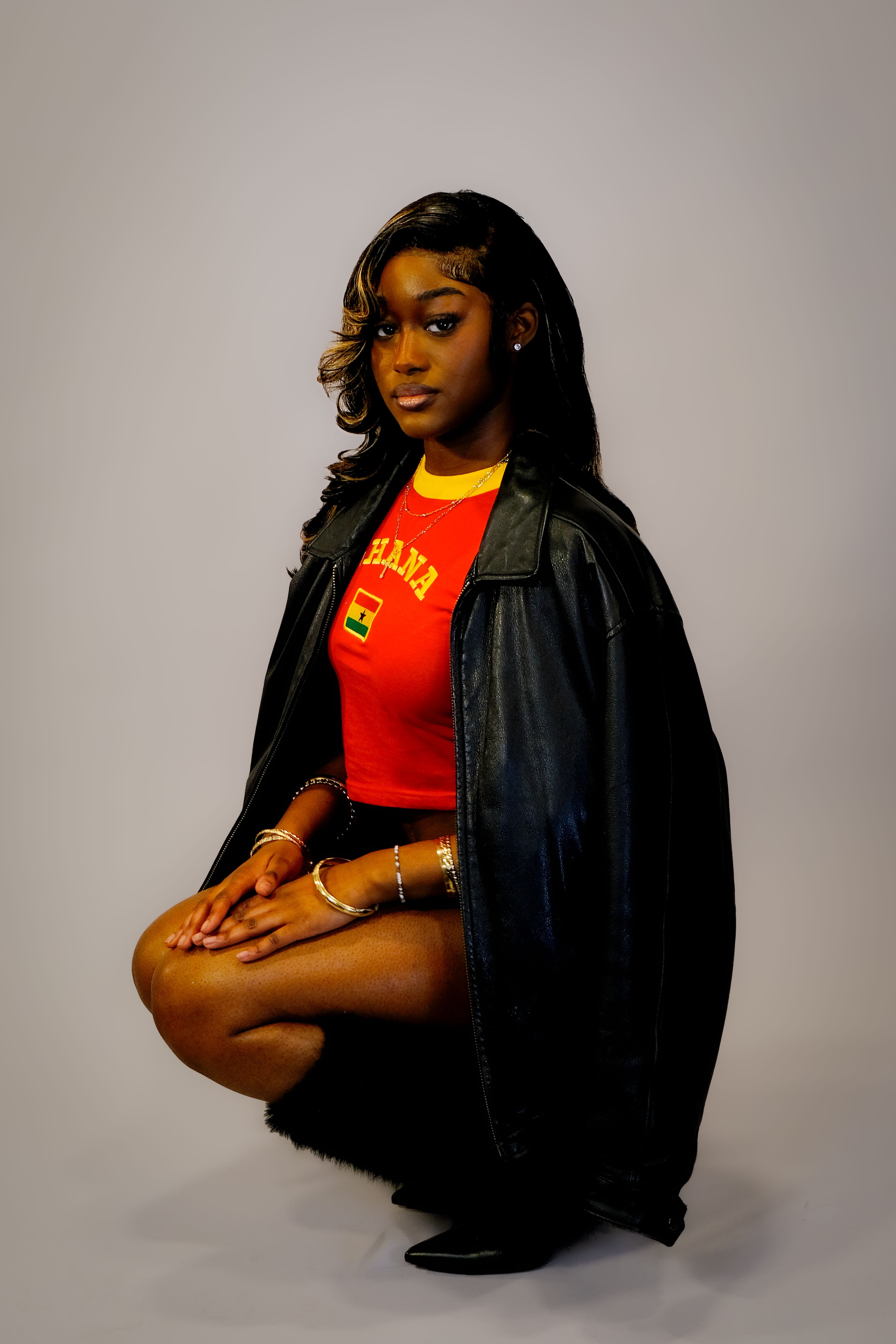Woman wearing a red shirt with a "GHANA" logo and black jacket on a gray background