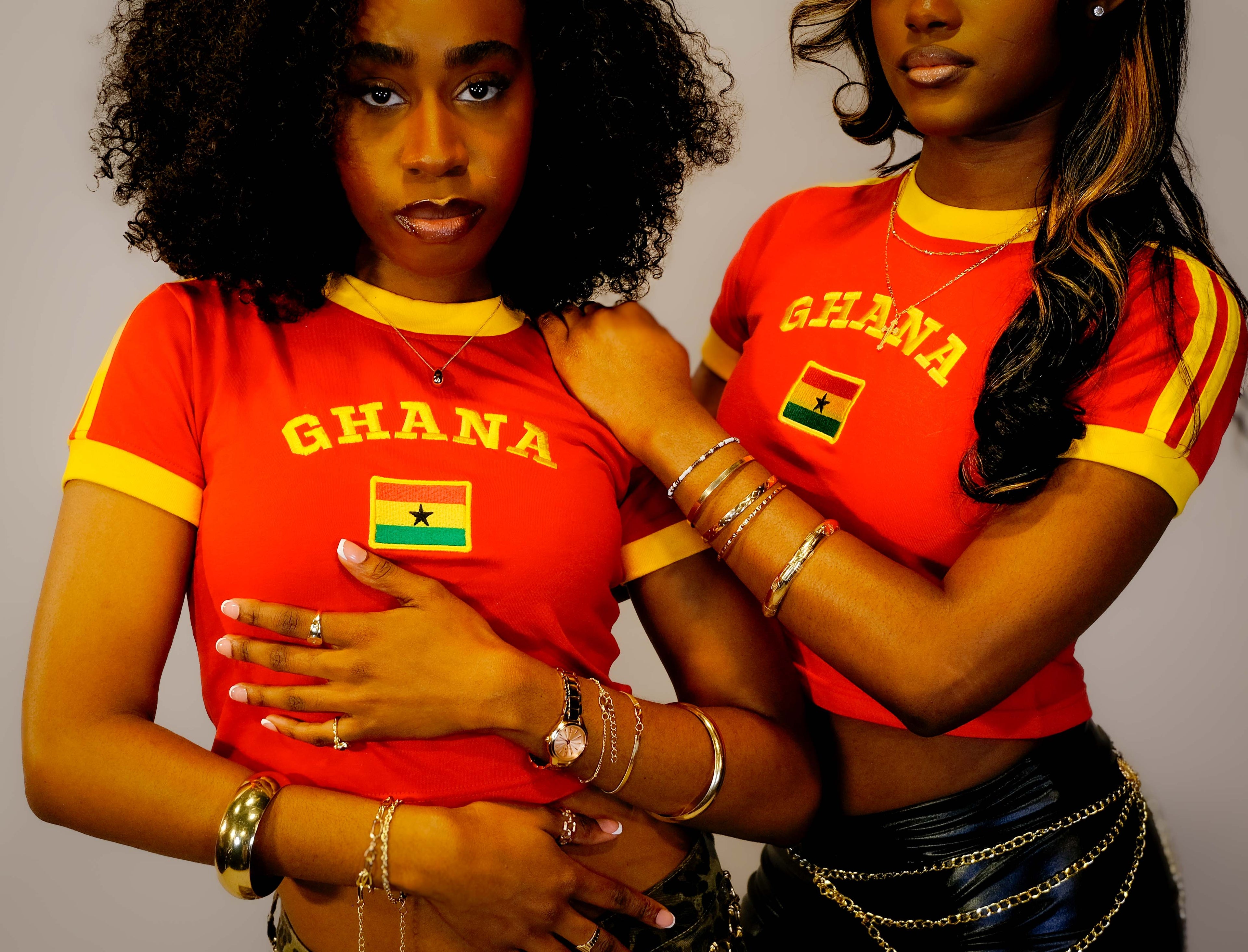 Two women wearing red 'Ghana' shirts with yellow accents on a plain background